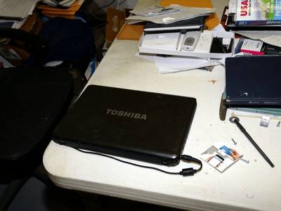 File:EFTA00002465 - Cluttered desk with a closed Toshiba laptop papers books and office supplies.jpg