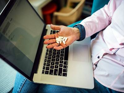 File:Individual holding white pills while working on a laptop in a modern home office during the day.jpg