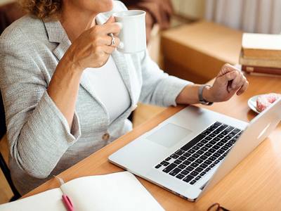 File:Professional woman enjoying coffee while working on laptop at a cozy desk in a well-lit room during morning hours.jpg