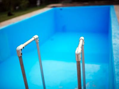 File:A vibrant blue swimming pool features white metal ladders against a clear sky.jpg