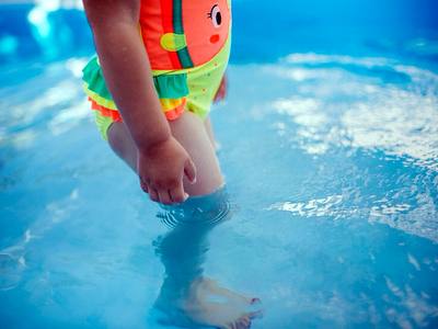 File:A young child stands in shallow water, enjoying the coolness of the pool while wearing a colorful swimsuit. The sunlight reflects off the water, creating a joyful atmosphere.jpg